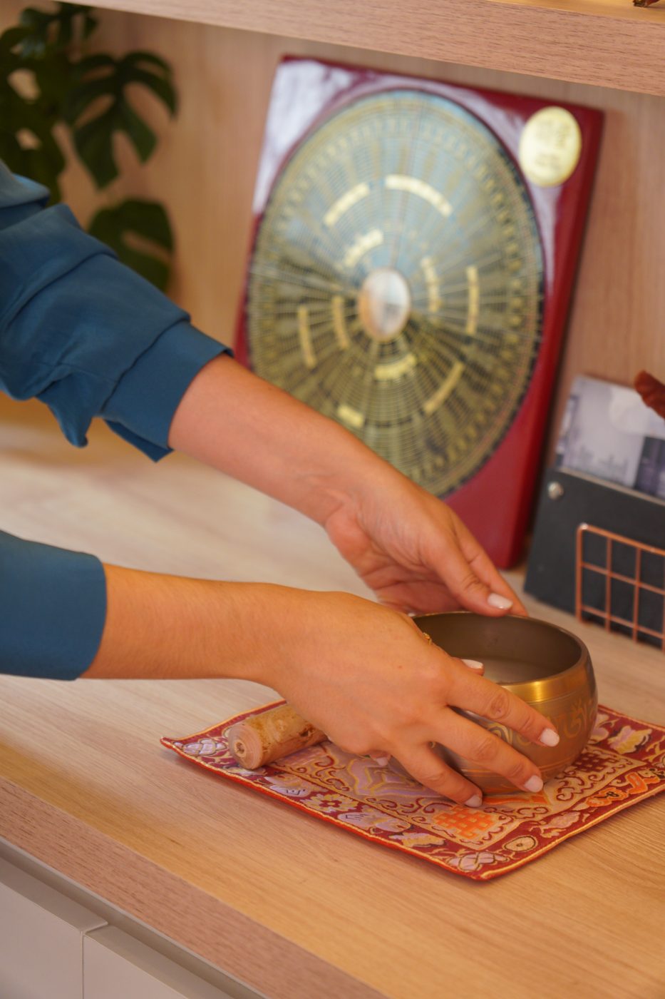 Mãos posicionando um sino tibetano diante de uma bússola Luo Pan sobre bancada de madeira